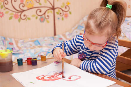 girl sitting at the table and draws paints on white paperの写真素材