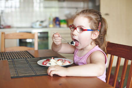 The girl sits on a chair at the table and eats berries. sunny day. Beautiful kitchen. Soft blurry backgroundの写真素材