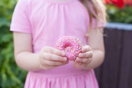 A little girl with glasses and a pink dress is eating a sweet donut.の写真素材