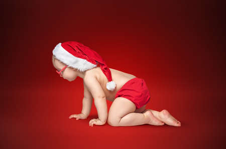 little baby with Santa hat and glasses crawling on rad background.の写真素材