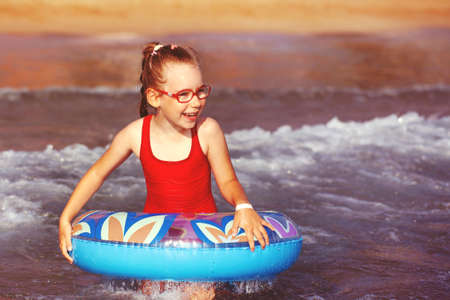 young girl in glasses plays in the water on an inflatable donut in a hot sunny summerの写真素材