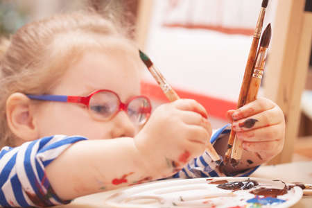 girl with glasses is considering a brush and paintの写真素材