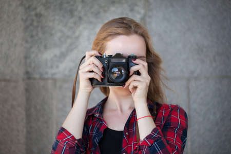 Girl in shorts and a red shirt in a cage, with a retro camera in her handsの写真素材