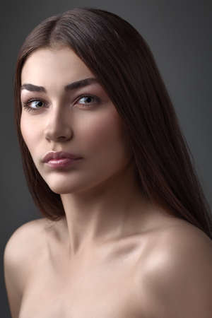 The beautiful girl poses in studio on a gray background. Fashion portrait. Make-up. Long hair