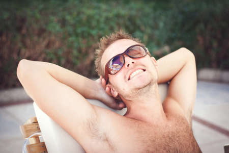 young man in sunglasses smiling lying on a sunbedの写真素材