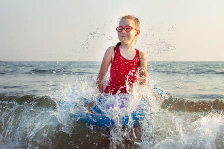 young girl in glasses plays in the water on an inflatable donut in a hot sunny summer