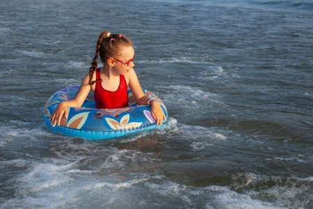 young girl in glasses plays in the water on an inflatable donut in a hot sunny summerの写真素材