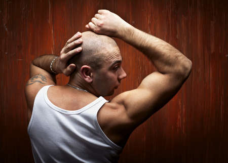 portrait of the bald sports person in a white shirt, before a red wall.