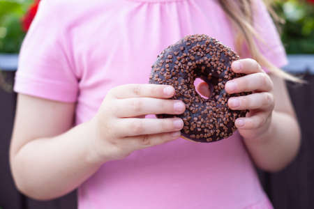 A little girl with glasses and a pink dress is eating a sweet donut.の写真素材