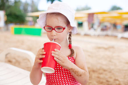 young funny girl in red glasses and swimsuit drinks from a glass on the beachの写真素材