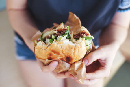 The girl is holding a big hamburger. Soft blurry background. life styleの写真素材