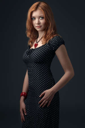 portrait of the young beautiful girl with red hair, in a black dress, on a dark backgroundの写真素材