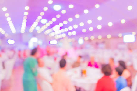blurred image of Large dining table set for wedding, dinner or festival event with beautiful lights decoration inside large hall with peopleの写真素材