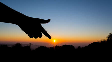 silhouette image of  hand point to the sun with sunset sky background to showing life target concept.の写真素材