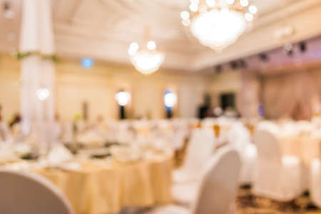 blurred image of Large dining table set for wedding, dinner or festival event with beautiful lights decoration inside large hall with people.の写真素材