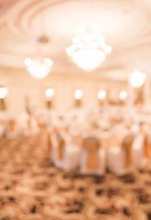 blurred image of Large dining table set for wedding, dinner or festival event with beautiful lights decoration inside large hall with people.の写真素材