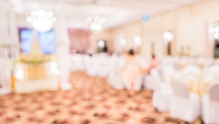 blurred image of Large dining table set for wedding, dinner or festival event with beautiful lights decoration inside large hall with people.の写真素材