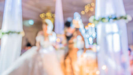 blurred image of Large dining table set for wedding, dinner or festival event with beautiful lights decoration inside large hall with people.の写真素材