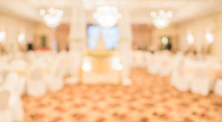 blurred image of Large dining table set for wedding, dinner or festival event with beautiful lights decoration inside large hall with people.の写真素材