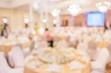 blurred image of Large dining table set for wedding, dinner or festival event with beautiful lights decoration inside large hall with people.の写真素材