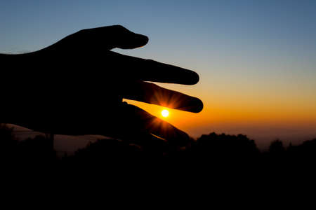 silhouette image of  hand point to the sun with sunset sky background to showing life target concept.の写真素材