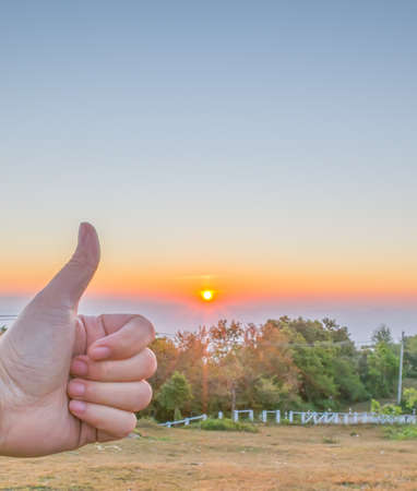 image of Thumb up means Good sign with sunset sky background.(focused on Thumb)の写真素材