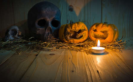 image of rotten Halloween pumpkin with candle light and dry grass. Wooden background.