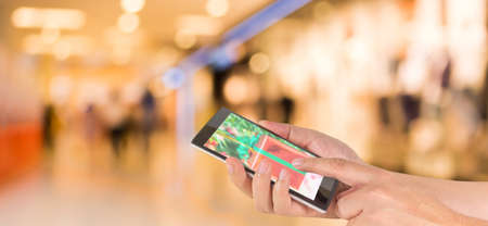 male hand is holding a modern touch screen phone and Blurred image of people walking at shopping...