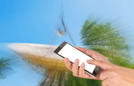 male hand is holding a modern touch screen phone and image of large sattelite dish  and blue sky in...