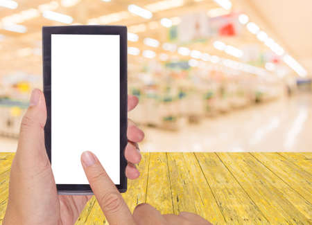 male hand is holding a modern touch screen phone and blurred image of supermarket for background usage .の写真素材