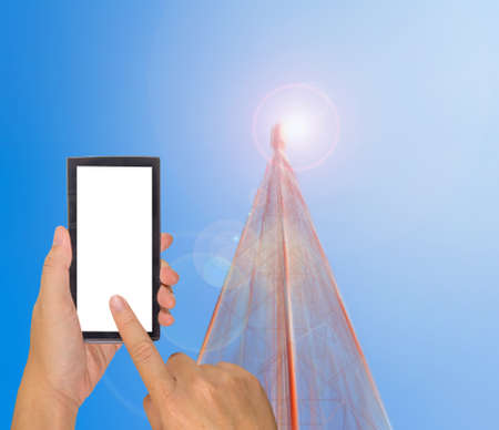 male hand is holding a modern touch screen phone and image of Tele-radio tower with blue sky for...