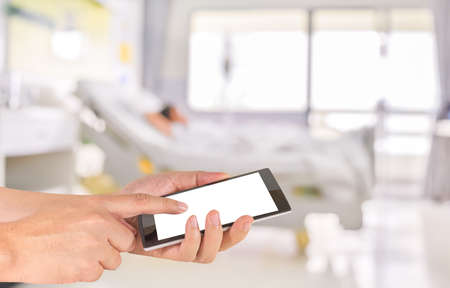 male hand is holding a modern touch screen phone and blurred image of Patient with drip in hospital...