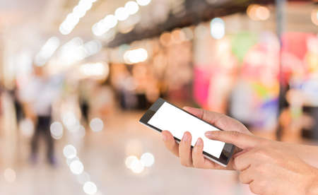 male hand is holding a modern touch screen phone and Blurred image of people walking at shopping mall , blur background with bokehの写真素材