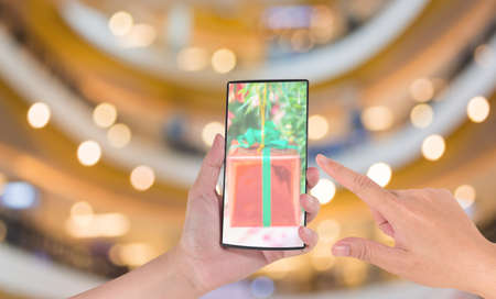 male hand is holding a modern touch screen phone and Blurred image of shopping mall .の写真素材