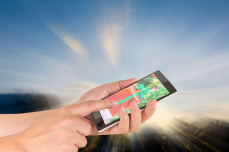 male hand is holding a modern touch screen phone and silhouette shot of coconut tree and sky in background .の写真素材