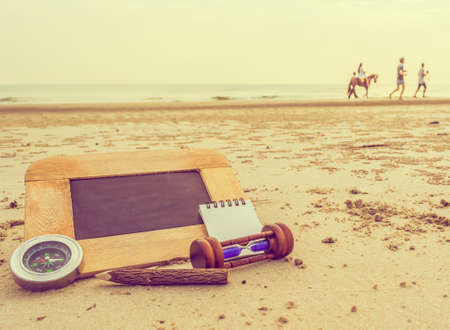journey concept vintage tone image of chalkboard and stationery items For creative idea with blur people riding horse and sea in background.(selective focus on chalkboard)の写真素材