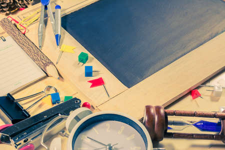 vintage tone image of wooden table top view of the chalk board with creative stationery items to...