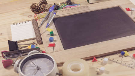 vintage tone image of wooden table top view of the chalk board with creative stationery items to...