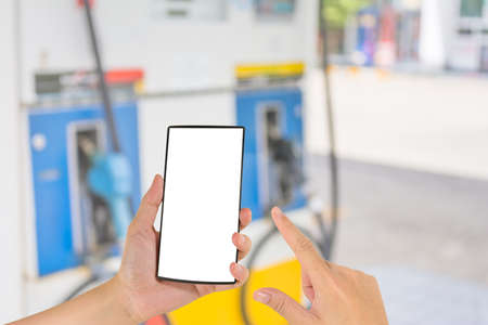 concept idea image of hand holding smart phone and gas station in background .