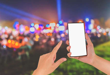 male hand is holding a modern touch screen phone and Blurred image of night festival for background usage .の写真素材