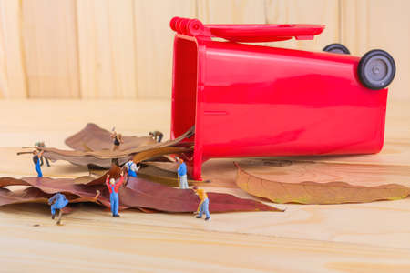 concept idea image of mini figure dolls worker collect dry leaves into the red recycle bin .(meaning as group of people help to keep environment safe)の写真素材