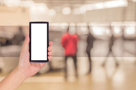 male hand is holding a modern touch screen phone and blur image of Commercially cars stand .