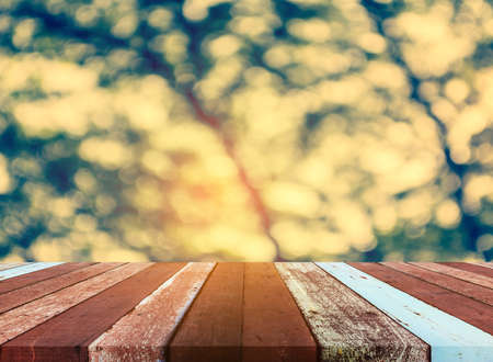wood table and blur image of Abstract Bokeh of green tree with sun for background usage.