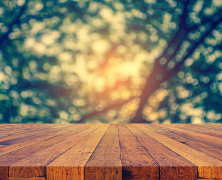wood table and blur image of Abstract Bokeh of green tree with sun for background usage.