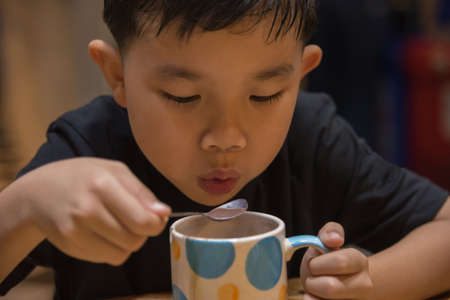 Young asian boy drink hot chocolate from cup in milk shop.の写真素材