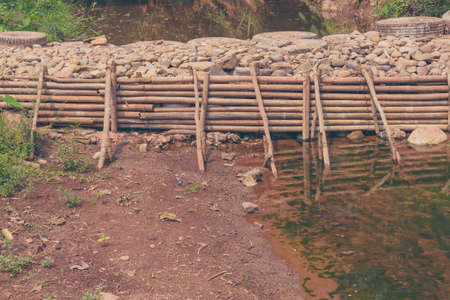 vintage tone image of man made weir(small dam) made from bamboo and rock across the river on day time.の写真素材