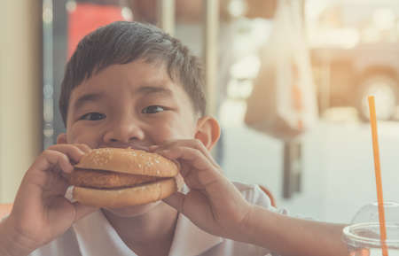 image of happy Asian boy eating hamburger in restaurant .の写真素材