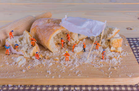 concept idea image of mini figure dolls as engineer team making French Baguette bread on slice board.の写真素材