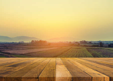 vintage tone image of wood table and rice field with sun and mountain in background.