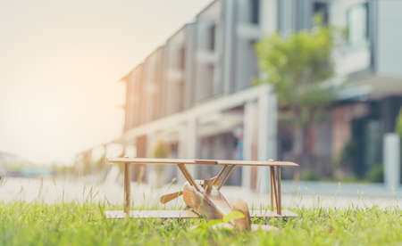 vintage tone image of wooden plane toy on grass field and blur townhouse in background.